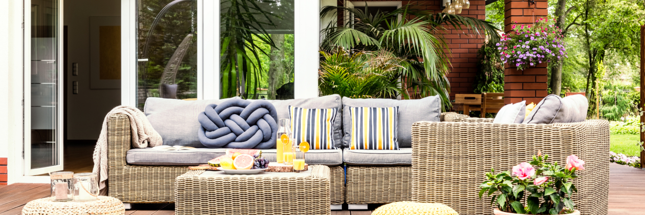Beige garden furniture with striped pillows on a wooden terrace with pink flowers and poufs