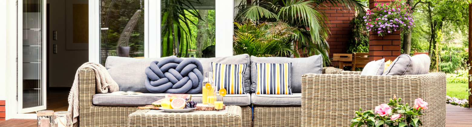Beige garden furniture with striped pillows on a wooden terrace with pink flowers and poufs